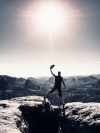 Man with arm outstretched celebrating sunset in mountains. hiker with hand up hold leather hat enjoy