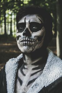 Close-up portrait of young man with spooky face paint in forest