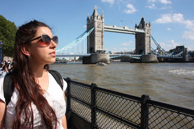 Young woman standing by railing at bridge against sky