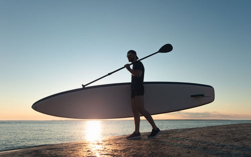 Man standing in sea against sky during sunset