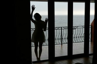 Silhouette woman standing by railing against sea