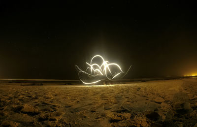 Light trails on beach against sky at night