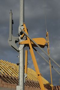 Low angle view of crane against cloudy sky at construction site