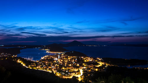 High angle view of illuminated city by sea against sky at night