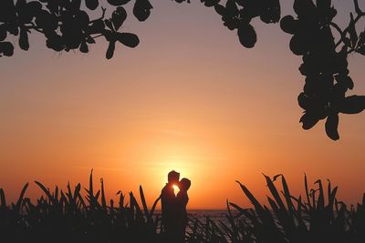 Silhouette couple kissing while standing at beach against orange sky during sunset