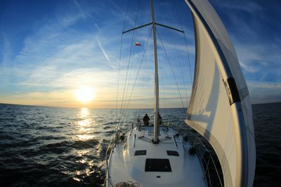 Close-up of sailboat sailing on sea against sky during sunset