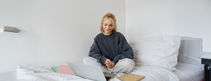 Portrait of young woman sitting on bed at home
