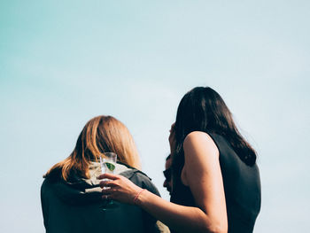 Rear view of women against clear sky on sunny day