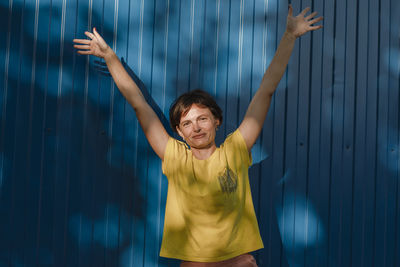 Joyful young brunette woman girl in casual clothes posing on blue wall background. rising hand