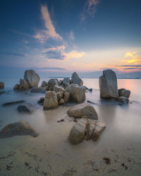 Rocks on sea shore against sky during sunset