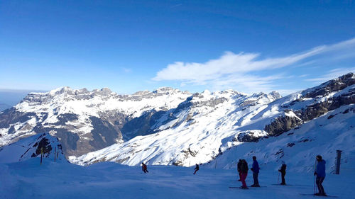 People skiing at snowcapped mountains against blue sky