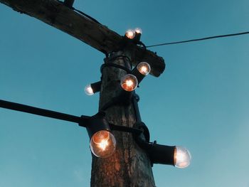 Low angle view of illuminated light bulbs on wood against sky