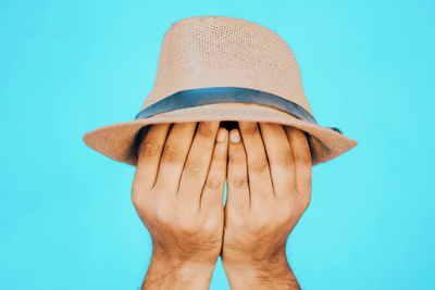 Close-up of hand holding hat against blue background
