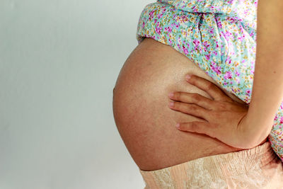 Midsection of pregnant woman touching abdomen while standing against wall