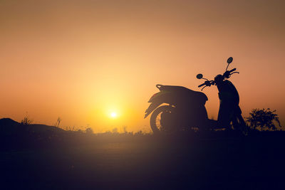 Silhouette motor scooter on land against sky during sunset