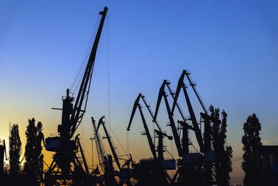 Low angle view of silhouette cranes against clear blue sky