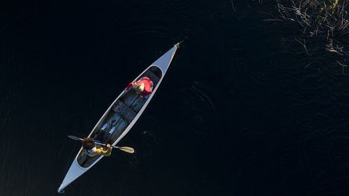 Young man paddling through oar while sitting with woman in canoe on river during sunset