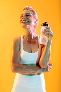 Young woman drinking water bottle against yellow background