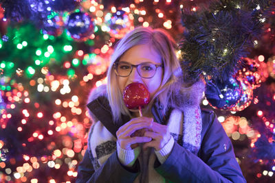 Portrait of young woman eating caramelized apple during christmas at night