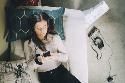 High angle view of female teenager using smart phone while lying on bed at home