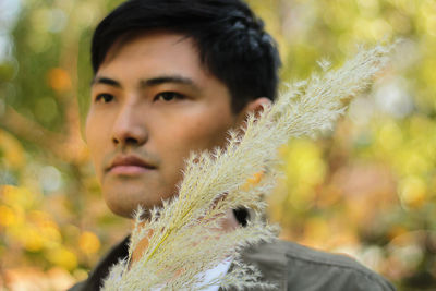 Young man holding plant looking away while standing outdoors