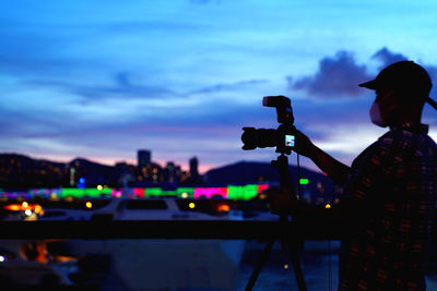 Man photographing illuminated lamp against sky at night