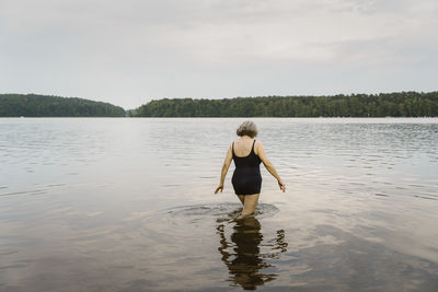 Rear view of senior woman walking in knee deep river