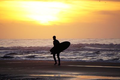 Silhouette man on beach against sky during sunset