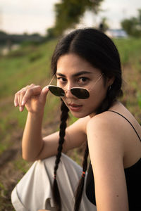 Portrait of young woman holding sunglasses on field