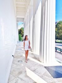 Full length of woman walking at colonnade against white wall