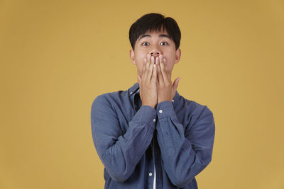 Portrait of young man standing against yellow background