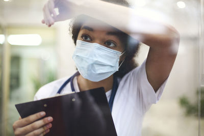 Nurse wearing mask looking away through glass