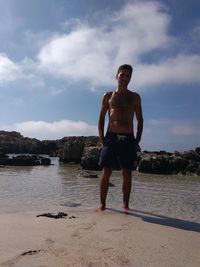 Full length of shirtless man standing at beach against sky