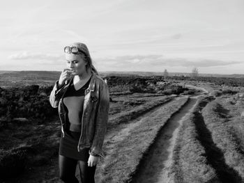 Young woman standing on field against sky