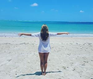 Rear view of woman with arms outstretched standing at beach against sea