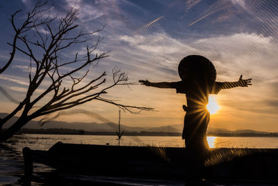 Silhouette woman standing at beach against sky during sunset