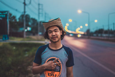 Portrait of young man standing on street in city at dusk