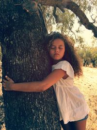 Girl with eyes closed hugging tree trunk