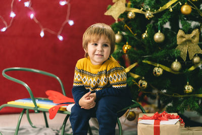 Smiling boy sitting by christmas tree