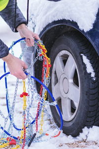 Cropped hands of person holding chains by snow covered car