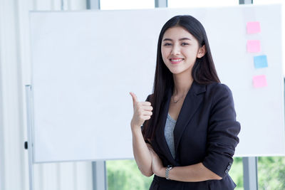 Portrait of smiling young woman standing against wall