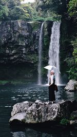 Woman standing on rock against waterfall