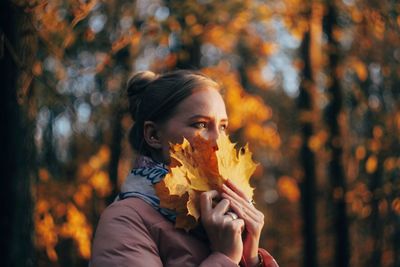 Portrait of young woman holding maple leaves during autumn