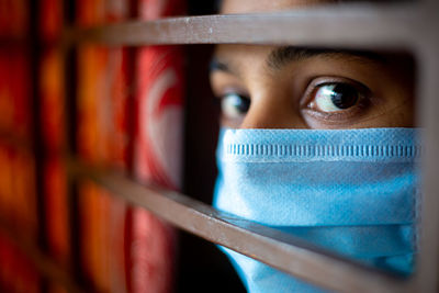 A bored asian young girl wearing a protective surgical face mask at looking through the window.