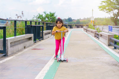 Little child girl to ride scooter in outdoor sports ground on sunny summer day. 