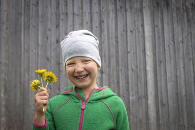 Portrait of smiling boy holding flower standing outdoors