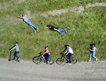 High angle view of man and woman riding bicycles by friends lying down on field