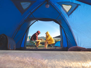 Asian couple sit front of tent camping around mountain lake