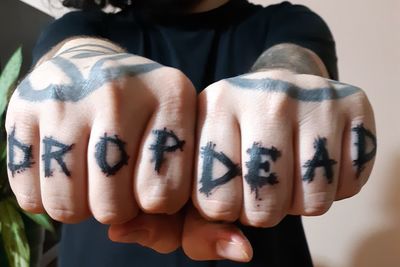 Midsection of young man showing tattoo on fingers at home
