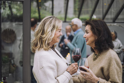 Smiling senior woman with wineglasses talking to female friends at dinner party